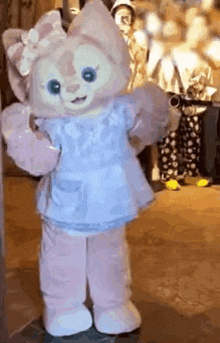 a stuffed animal wearing a blue dress and apron is standing on the ground .