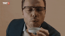 a man wearing glasses and a suit is holding a container with trt1 written on the bottom right corner