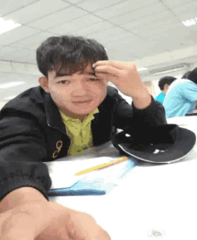 a young man is sitting at a table with a hat and pencils