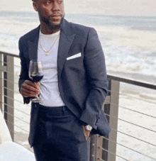 a man in a suit is holding a glass of wine while standing on a balcony .