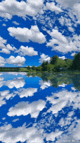 a blue sky with white clouds and trees reflected in a lake