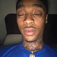 a man wearing a blue shirt and a necklace is sitting in a car with his eyes closed .