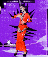 a woman in a red latex dress and black spikes on her head is standing on a stage .