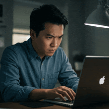 a man in a blue shirt is working on an apple laptop