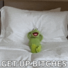 kermit the frog is sitting on a bed with the words `` get up bitches '' above him .