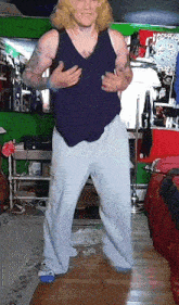 a man in a blue tank top and white pants is dancing in a room
