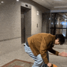 a man in a brown jacket is bending over in front of an elevator in a building