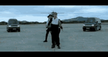 a group of people are standing in front of a helicopter and vans .