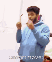 a man wearing a blue hoodie is holding a pair of glasses and says smartmove .