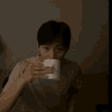 a man is sitting on a couch holding a cup of coffee and looking at the camera .