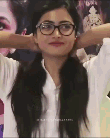 a woman wearing glasses holds her hands behind her head .