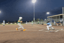 a baseball game is being played at night with a sign that says ' a & a ' on it