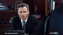 a man in a suit and tie is sitting in front of a laptop with #lawandorder written on the bottom