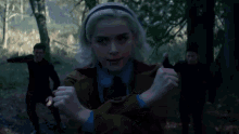 a woman in a black coat stands in a dark forest