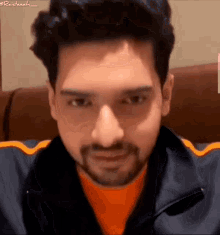 a man with a beard is sitting on a couch looking at the camera .