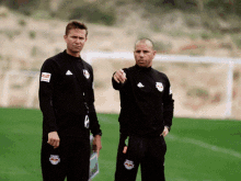 two men are standing on a soccer field and one has a red bulls logo on his pants