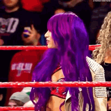 a wrestler with purple hair is standing in a ring .