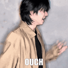 a man wearing a tan jacket has the word ouch written on his chest