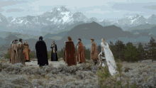 a group of people are standing in a field in front of mountains