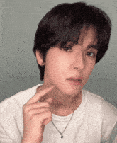 a young man wearing a white t-shirt and a black necklace looks at the camera