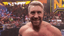 a shirtless wrestler smiles in front of a crowd and a sign that says nmt