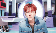 a young man with red hair and a denim jacket looks at the camera