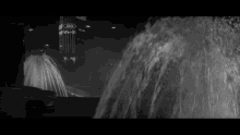 a black and white photo of a car in front of a fountain with a building in the background that says ' a '