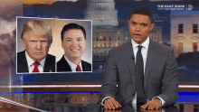 a man in a suit and tie stands in front of a screen that says the daily show