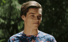 a young man wearing a blue shirt with flowers on it is smiling .