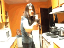 a man with long hair is standing in a kitchen holding a sword
