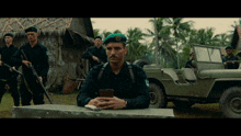a man wearing a green beret with a gold emblem on it sits in front of a jeep