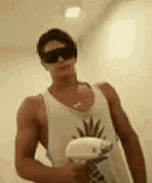 a man wearing sunglasses and a pineapple tank top is holding a pineapple .
