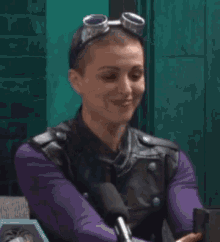 a woman wearing goggles and a leather jacket is sitting in front of a microphone and smiling .