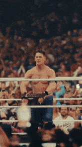 a shirtless wrestler stands in the middle of a ring with a crowd watching