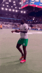 a soccer player in green shorts and a white shirt is dancing on the field