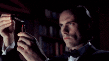 a man in a tuxedo is holding a red lipstick in his hands