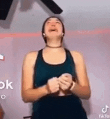 a woman in a blue tank top is laughing while holding a cell phone in her hands .