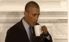 obama is drinking a cup of coffee while wearing a suit and tie .