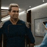 a man in a superhero costume is standing in a hallway looking at a phone .