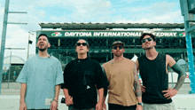 a group of men standing in front of a daytona international speedway sign