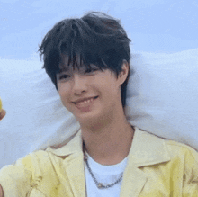 a young man is laying on a bed wearing a yellow jacket and a white t-shirt and smiling .