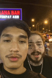 two men are posing for a photo in front of a sign that says lana bar tempat asik
