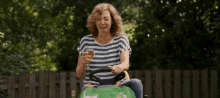 a woman is sitting on a lawn mower drinking a glass of wine .