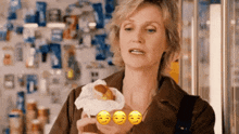 a woman is holding a hot dog in her hand with three smiley faces around her .