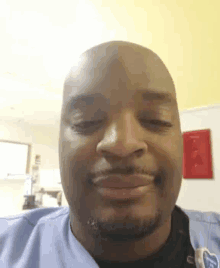 a bald man with a beard is smiling and wearing a scrub top with the letter t on it