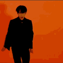 a man in a black suit is standing in front of an orange wall .