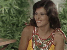 a woman wearing a yellow top with a red and white floral pattern smiles