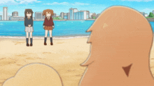 a cartoon of three girls standing on a beach with buildings in the background