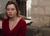 a woman sitting on a couch wearing a red sweater and a necklace