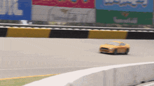 a yellow car is driving on a race track with a sign in the background that says alberta